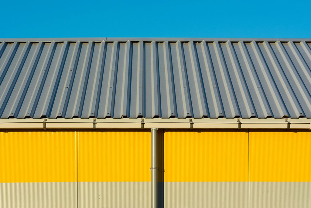 Photo of a yellow warehouse wall with a corrugated metal roof under a clear blue sky.